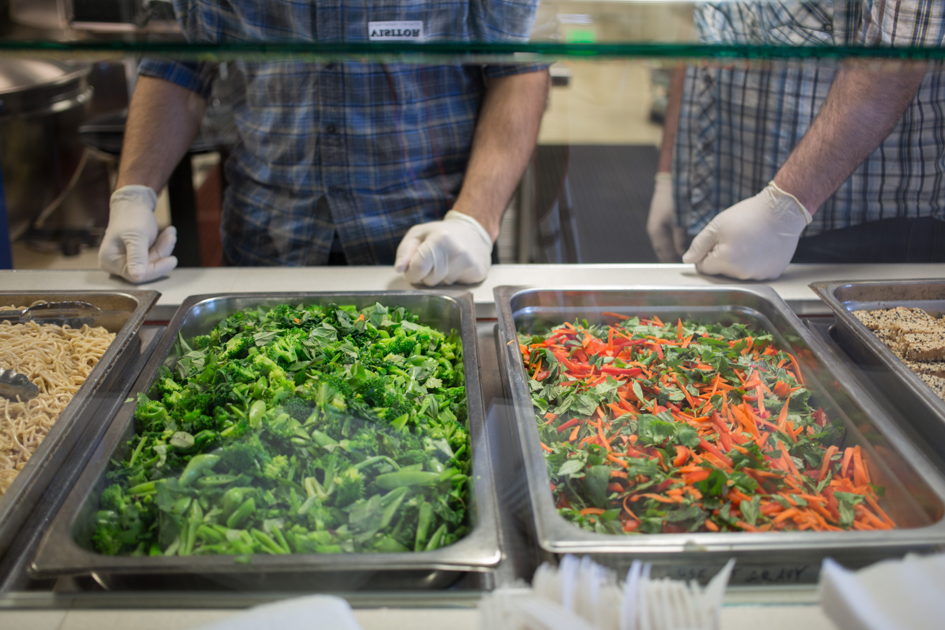 image is of two pans of vegetables, with a pair of hands wearing gloves above them